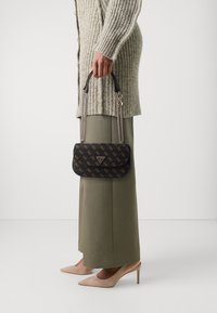 Zwarte handtas met patroon en kettinghandvaten, met gouden logo accenten. Gedragen met een lange, geribbelde trui en wijde broek.