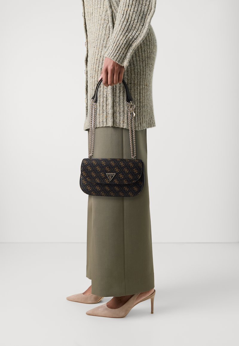 Zwarte handtas met patroon en kettinghandvaten, met gouden logo accenten. Gedragen met een lange, geribbelde trui en wijde broek.