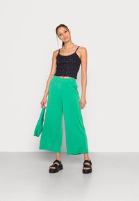 Top cropped azul marinho com estampado floral vermelho; calças largas verdes; sandálias pretas; mala tote verde a condizer. Tecido suave, design casual.