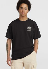 Sort kortærmet T-shirt med rund hals, der har hvid grafisk tekst og blomsterdesign på venstre brystområde. Lavet af bomuldsstof, afslappet pasform.