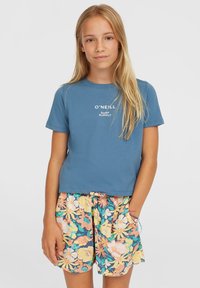 Blaues kurzärmliges T-Shirt mit weißem Druck "O'Neill Surf Supply", kombiniert mit bunten Shorts im floralen Muster in Gelb und Blau.