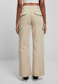 Pantalones cargo beige de corte holgado, con dos bolsillos laterales y dos bolsillos traseros con solapa, fabricados en resistente material de algodón.