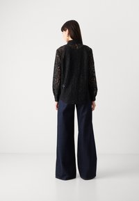 Black lace blouse with long sleeves, featuring a floral pattern, paired with wide-leg dark denim trousers. Minimalist design, textured fabric.