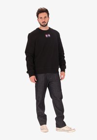 Felpa nera con scollatura a girocollo e una grafica colorata sul petto, abbinata a pantaloni in denim scuri e sneakers bianche.