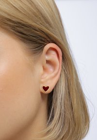 Boucles d'oreilles en métal doré en forme de cœur, dotées d'une surface en émail rouge foncé. Le design est petit et se fixe confortablement sur le lobe de l'oreille.