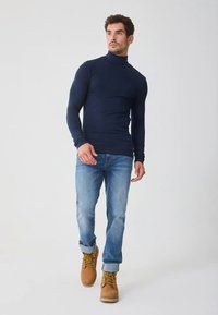 Tamnoplava rolka s dugim rukavima uparena sa svijetloplavim trapericama i smeđim čizmama s vezicama, karakterizirana uskim krojem i glatkim, rastezljivim materijalom.