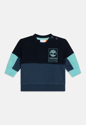Sweatshirt bleu marine avec des accents bleu clair. Il présente un col rond, des manches longues et un logo imprimé sur la poitrine. Comprend des boutons-pression.