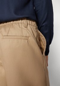 Khaki byxor med elastisk midja, sidofickor och en bakficka. Slät, vävd textur. Matchas med en marinblå skjorta med lång ärm.