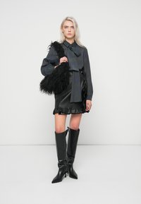 Musta nahkahame rypistetyn helman kanssa, yhdistettynä tummaan ruudulliseen puseroon ja korkeisiin mustiin korkokenkiin. Malli pitää käsissään mustaa sulkahandbagia.