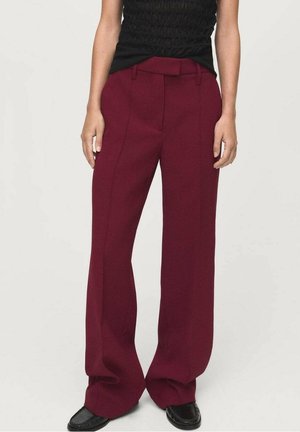 Vrouw draagt hooggetailleerde, wijde bordeauxrode broek met plooien aan de voorkant en zwarte loafers, gecombineerd met een mouwloos zwart topje.