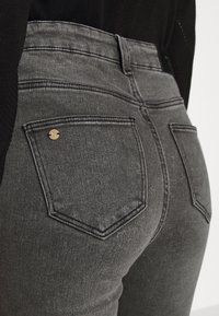 Jeans de mezclilla gris con un diseño ajustado, que cuentan con costuras de doble puntada, dos bolsillos traseros y un acento de logo metálico.