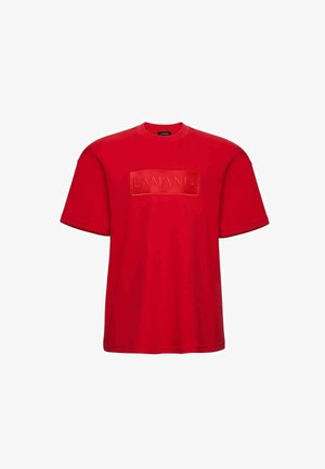 Czerwona bawełniana koszulka z krótkim rękawem, z wypukłą naszywką z logo "LAMANIA" na przodzie. Klasyczny okrągły dekolt i luźny krój.