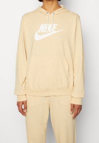 Béžová bavlněná mikina s kapucí a velkým bílým logem Nike, se šňůrkami, kapsou vpředu, dlouhými rukávy a vroubkovanými manžetami a lemováním.