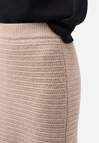 Närbild på en beige ribbad stickad kjol som bärs med en instoppad svart tröja, visar textur och midjedetaljer.