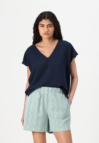 Haut bleu marine à col en V avec des manches courtes, associé à un short vert clair avec des motifs en zigzag, fabriqué dans un tissu léger et texturé.
