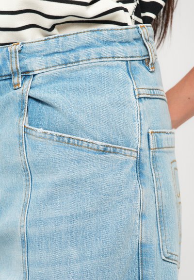 Close-up of light blue denim jeans pocket with orange stitching worn with a black and white striped shirt.