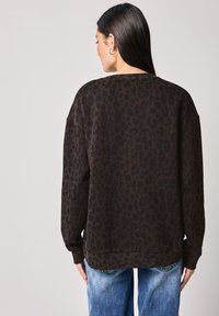 Sweatshirt en imprimé léopard marron foncé avec des taches noires, doté d'un col rond et d'un ourlet côtelé, associé à un jean en denim bleu clair.