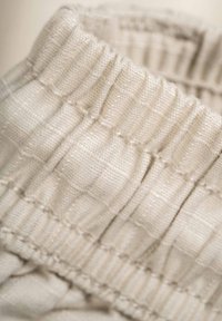 Cream-colored fabric with a textured, ribbed surface and gathered elastic at the top, showcasing a soft, woven pattern and fine stitching.