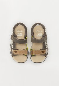 Bruna barnsandaler med två justerbara kardborreband, beige innerfoder och en gummisula med en färgglad accent.