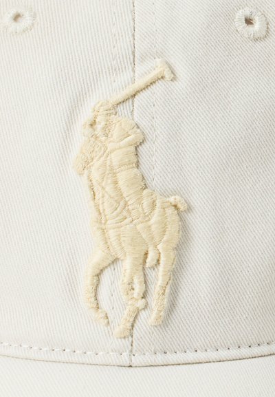 Bombažna kapa za bejzbol v svetli bež barvi s vezenim logotipom polo igralca kremne barve na sprednji strani. Ima šest prezračevalnih očes.