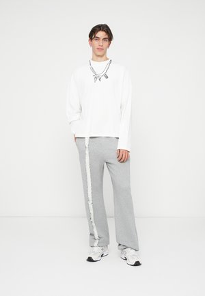Witte langzamige blouse met zwarte hangerafbeelding, gecombineerd met grijze sweatpants met een textuurwitte stripe, en witte sneakers.