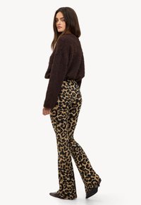 Suéter marrón esponjoso combinado con pantalones acampanados de estampado de leopardo. Los pantalones presentan manchas negras sobre un fondo marrón claro, completados con zapatos oscuros.