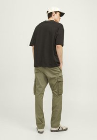 Zwarte t-shirt met korte mouwen, olijfgroene cargobroek en lichte sneakers. De outfit heeft een ontspannen pasvorm met cargozakken en een pet.