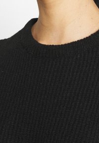 Svart ribbat stickat tröja med rundad halsringning. Tyget är strukturerat och mjukt, vilket visar fina detaljer i det ribbade mönstret.