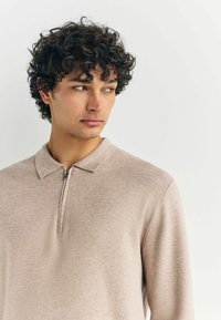 Ljusbeige zip-up polo tröja med en mjuk textur, som har en krage och en subtil ribbad design. Passformen är skräddarsydd.