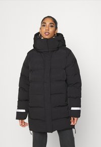 Chaqueta de plumas negra con diseño acolchado, cuello alto y detalles reflectantes en las mangas. Con capucha, ajuste relajado y cierre de cremallera.