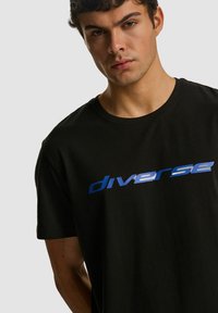 Czarny bawełniany t-shirt z krótkimi rękawami, z niebieskim napisem "diverse" na klatce piersiowej. Okrągły dekolt i luźny krój.