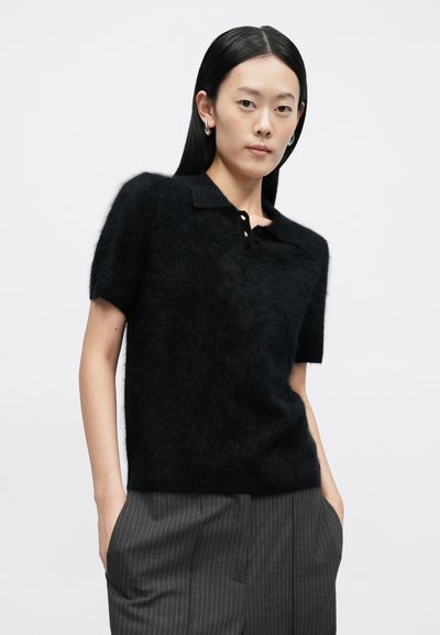 Sort poloshirt med korte ærmer i en fuzzet tekstur med krave og tre-knaps lukning. Kombineret med grå bukser med smalle striber.