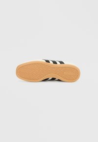 Λευκό αθλητικό παπούτσι με μαύρες ρίγες, λαστιχένια σόλα με υφή κυματιστού μοτίβου και ανάγλυφο λογότυπο. Άνω όψη που δείχνει το σχέδιο της σόλας.