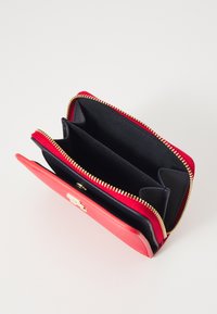Portefeuille rectangulaire avec un extérieur corail et un intérieur noir. Comprend une fermeture éclair dorée et plusieurs compartiments pour cartes et espèces.