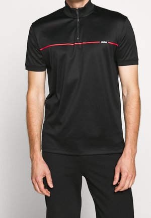 Man wearing a black short-sleeve zip-up shirt with a red horizontal stripe and white "HUGO" logo on the chest.