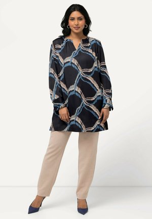 Langes, dunkles Tunika mit blauem und cremefarbenem abstraktem Muster; leichtes Material; kombiniert mit beigen Hosen und blauen Absätzen; lockere Passform.