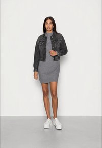 Jachetă din denim negru peste o rochie gri cu mânecă scurtă, asociată cu adidași albi. Jacheta are buzunare clasice și un design scurt.