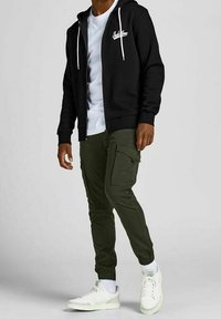 Sort lynlås sweatshirt med hvide snore, parret med grønne cargo bukser med sidelommer og elastiske manchetter. Båret med hvide sneakers.