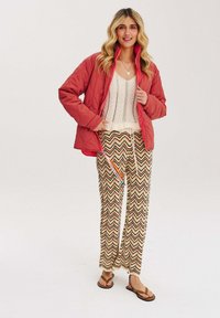 Czerwony pikowany kurtka, kremowy sweter i wzorzyste szerokie spodnie z zygzakowatym wzorem w ziemistych odcieniach. Brązowe klapki dopełniają strój.