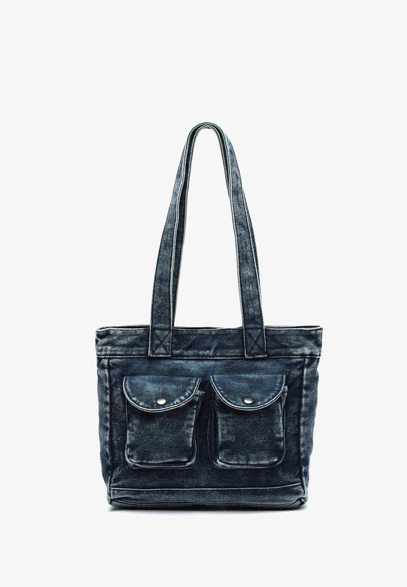 Sac fourre-tout en denim bleu foncé avec deux poches avant à rabat boutonné et longues poignées doubles sur fond blanc.