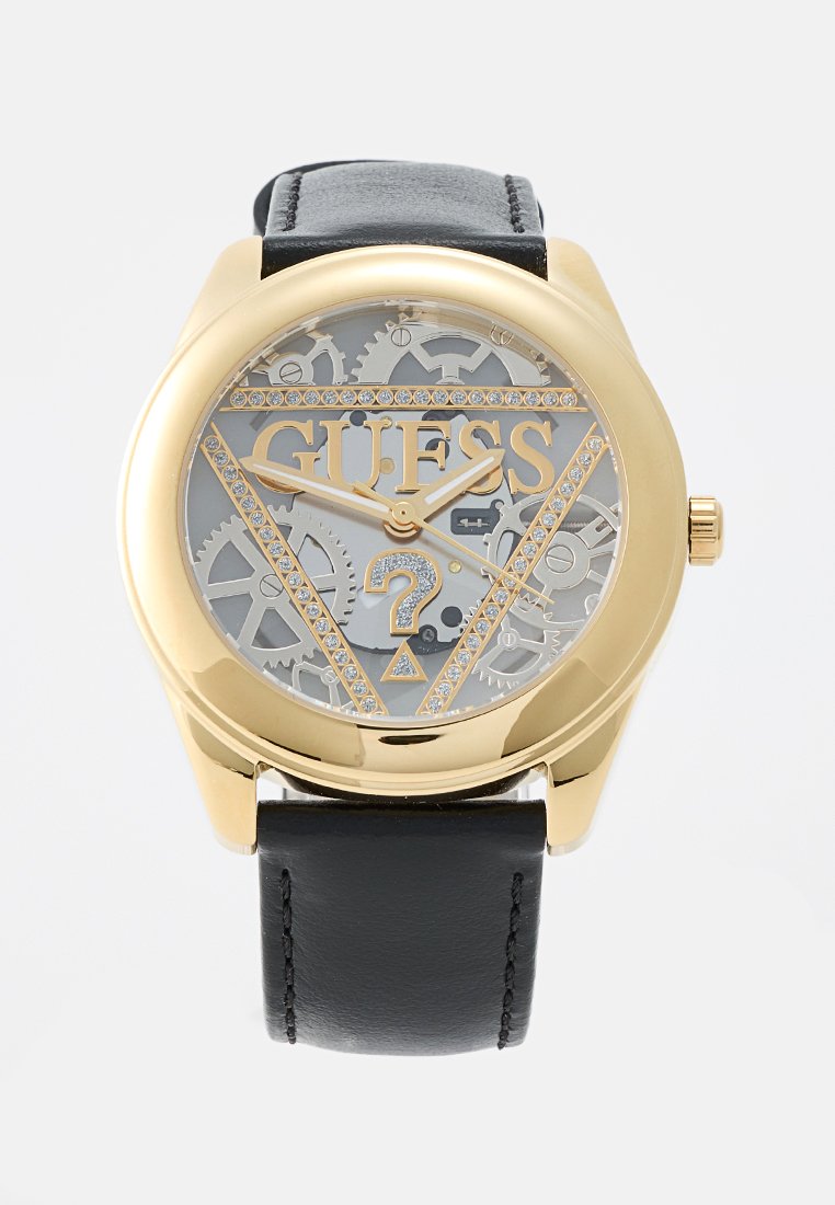 Orologio in tonalità oro con un quadrante grigio trasparente che mette in mostra gli ingranaggi. Presenta un cinturino in pelle nera e un logo a triangolo "GUESS" con accenti di gemme.