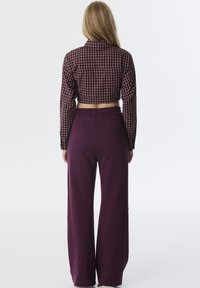 Afgeknotte geruite blouse in paars en bruin, gecombineerd met wijde paarse broek. De stof ziet er zacht uit met een elastische tailleband.