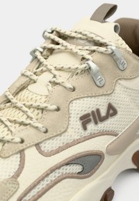 Κρεμ και μπεζ αθλητικό παπούτσι με υφασμάτινο άνω μέρος που συνδυάζει δίχτυ και σουέτ, διακοσμημένο με γκρι σχέδιο και ασημένια στοιχεία για τα κορδόνια.