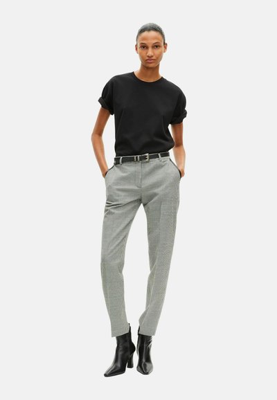 Zwart T-shirt met korte mouwen gecombineerd met grijs-wit geruite broek, voorzien van een zwarte riem en strakke zwarte enkellaarsjes.