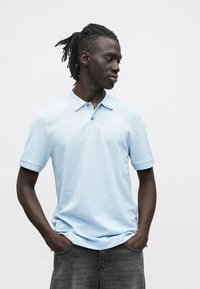 Svetlomodré bavlnené polotričko s golierom, krátkymi rukávmi, dvoma gombíkmi a malým logom na hrudi.