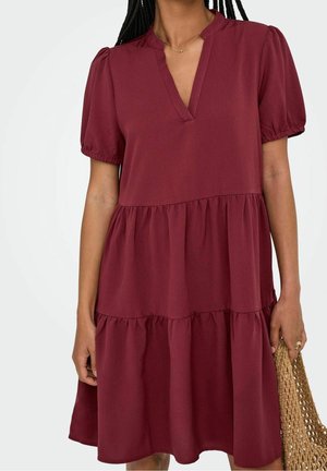 Bordowa sukienka warstwowa z dekoltem w serek, bufkami i miękką, teksturowaną tkaniną. Projekt posiada trzy plisowane warstwy.