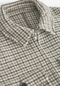Uldblandet skjortejakke i et houndstooth-mønster. Grå og beige farver med lynlås lukning og to forlommer. Struktureret stof.