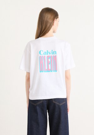 White cotton t-shirt featuring a colorful "Calvin KLEIN" graphic in pink and blue on the back. Relaxed fit with short sleeves.