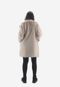 Lys beige kunstpelsjakke med en rund krave, lange ærmer og en løs pasform. Båret over sorte leggings og ankelstøvler.