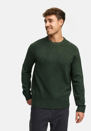 Vihreä villaneule, jossa on pyöreä kaula-aukko, ribbireunukset ja helma. Materiaali on pehmeä ja hieman karhea, mikä tarjoaa rennon ilmeen.